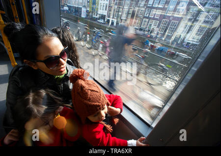 Jungen asiatischen Mutter reisen mit der Straßenbahn durch die Innenstadt von Amsterdam mit ihren zwei kleinen Töchtern auf dem Schoß Stockfoto
