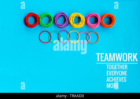 Teamwork Konzept. Gruppe von farbigen Gummiband auf blauem Hintergrund mit Word Teamarbeit, Zusammen, jeder, erzielt und mehr Stockfoto
