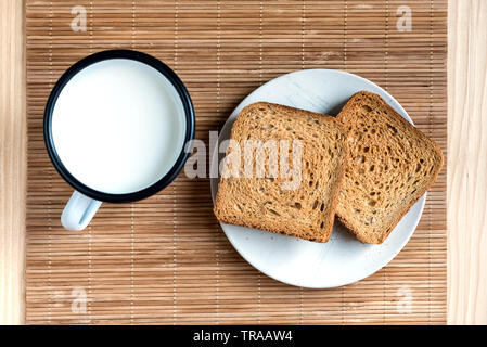 Zwei Scheiben Toast Brot und Zinn Becher Milch auf einem Holztisch, Setup Stockfoto