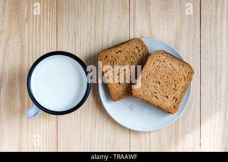 Zwei Scheiben Toast Brot und Zinn Becher Milch auf einem Holztisch, Setup Stockfoto