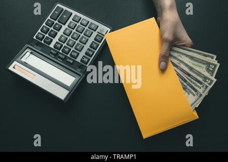 Auf dem schwarzen Leder Schreibtisch ein Rechner, das Mädchen hält in ihrer Hand ein gelber Umschlag mit Geld, Lohn für die Arbeit. Stockfoto
