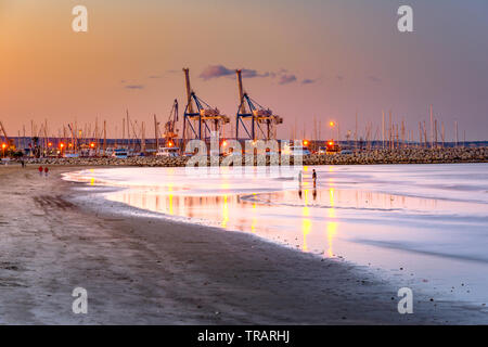 Krane bei Sonnenuntergang mit Sandstrand und Reflexionen im Vordergrund Hafen von Larnaca, Zypern Insel. Stockfoto