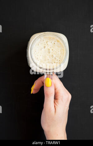 Woman's Hand mit einem Glas Glas Becher gefüllt mit Bananen Smoothie, Ansicht von oben. Stockfoto