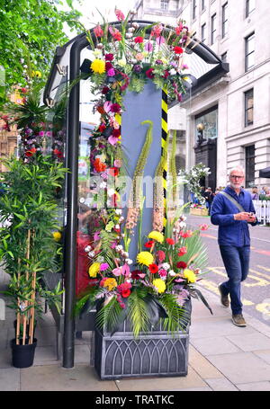 Von Manchester King Street Festival und Flower Show eröffnet für zwei Tage am 1. Juni 2019, Performance, Musik und kreative Blumenarrangements. Das Festival ist zu einem Retro 60er's Theme. Ein Mann hinter einer Bushaltestelle auf der King Street, die mit Blumen geschmückt wurde. Stockfoto