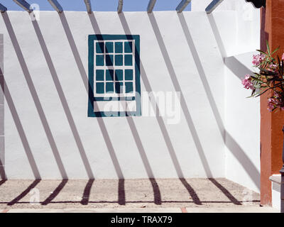 Starke Schatten von einem Metallgitter eine grafische Muster, die auf eine weiße Wand, diagonal von links oben nach rechts unten, in der Mitte der Wand ein Fenster Stockfoto