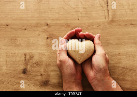 Erwachsene männliche Hand Holz- förmige Herz über Tabelle Stockfoto