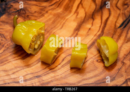 Gebeizt Golden griechische Paprika, pepperoncini oder Friggitelli (süßen italienischen Chili) auf natürlichen Holz Schneidebrett. Capsicum annuum. Stockfoto