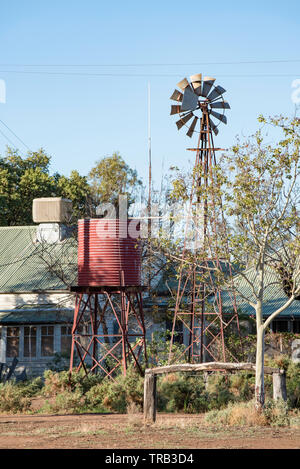 Morgensonne auf einem alten Wassertank, Windmühle und Bauernhaus im Nordwesten von NSW, Australien. Im Vordergrund ist eine alte Zaun für ruhende Pferde Stockfoto