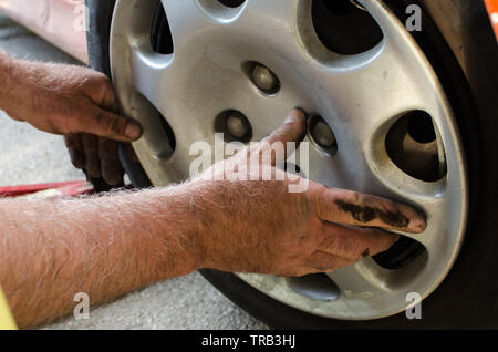 Mechaniker mit schmutzigen Händen Austausch des Kunststoff Radkappen nach Festsetzung der Reifen, extreme Close up, selektiven Fokus Stockfoto