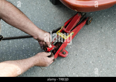 Automechaniker nimmt einen alten roten Auto Jack ein Reifen auf der Straße zu ändern, in der Nähe Stockfoto