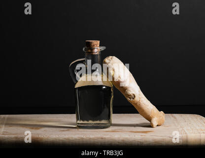 Ingwer öl Flasche mit Ingwer Wurzel auf Holz Schneidebrett. Gesunde Ernährung Konzept. Stockfoto