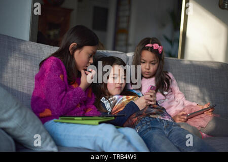 Drei junge asiatische Mädchen auf dem Sofa sitzen zusammen spielen auf Ihrem mobilen Gerät zu Hause faulenzen Stockfoto