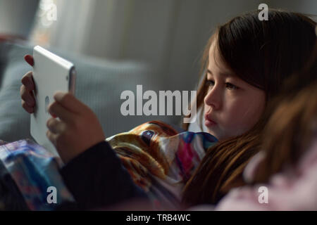 Drei junge asiatische Mädchen auf dem Sofa sitzen zusammen spielen auf Ihrem mobilen Gerät zu Hause faulenzen Stockfoto