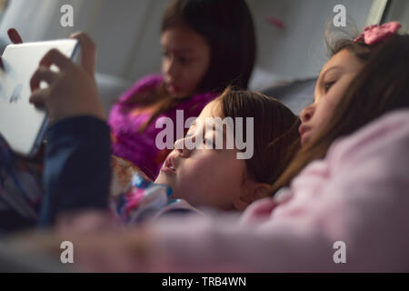 Drei junge asiatische Mädchen auf dem Sofa sitzen zusammen spielen auf Ihrem mobilen Gerät zu Hause faulenzen Stockfoto