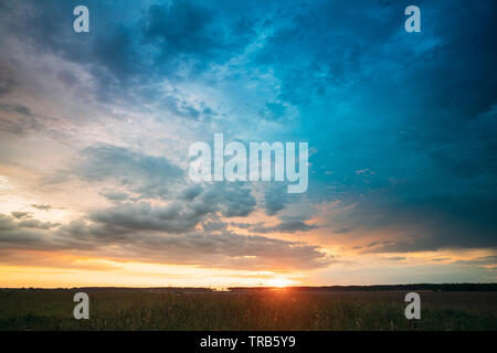 Frühling Sommer Wiese am Abend Sonnenuntergang Sonnenaufgang. Natürliche helle Dramatischer Himmel in verschiedenen Farben über Landschaft Wiese Landschaft. Landwirtschaftliche Flächen Stockfoto