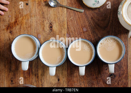 Vier Tassen mit spicy Chai Tee zum Trinken auf hölzernen Tisch bereit, hohe Betrachtungswinkel Stockfoto