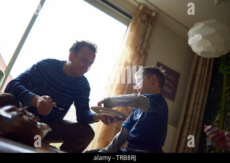 Vater helfen, seine netten jungen Sohn sein Mittagessen im Wohnzimmer zu essen Stockfoto