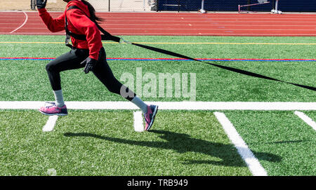 Ein High School Jugendmädchen tragen ein Rotes Sweatshirt, spandex und Handschuhe zieht einen Schlitten über den Rasen im Winter Leichtathletik Praxis. Stockfoto