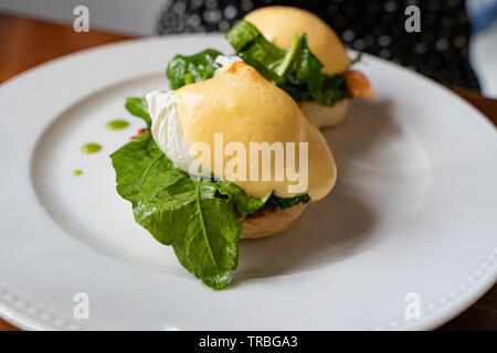 Ei Benedikt mit Lachs und frischem Spinat unter Sauce Hollandaise serviert auf einem weißen Teller Stockfoto