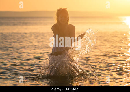 Schöne junge schwangere Frau mit weißen nassen Kleid entspannen Sie auf den Felsen in der Nähe des Meerwassers. Sommer bei Sonnenuntergang. Konzept Liebe und Schwangerschaft Stockfoto