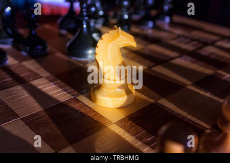 White Knight bleiben gegen den vollen Satz von schwarzen Schachfiguren. Nahaufnahme von einem Schachbrett mit Holz auf dem Tisch in der Sonne, ein Spiel der Lichter. Stockfoto