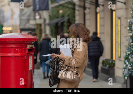 London, Großbritannien - 17, Dezember 2018: Frau drop Buchstaben in der Farbe Rot die traditionelle viktorianische British Briefkasten stehend auf der London Street. Stockfoto