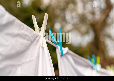 Weiße Kleidung hingen auf einer Wäscheleine zum Trocknen und befestigt die Wäscheklammern im hellen warmen sonnigen Tag. Garten der Hintergrund verschwommen. Stockfoto