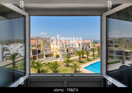 Durch geöffnete Fenster mit Blick auf die geschlossenen Bereich der Urbanisierung mit gepflanzten Palmen auf grünem Rasen rund um Schwimmbad mit blauen Wasser Stockfoto