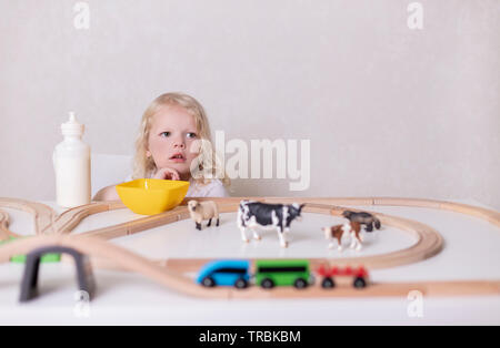 Kleinen Niedlichen baby boy (3 Jahre) trinkt Milch mit Cookies und spielt in den hölzernen Bahnhof in der Tabelle festgelegt. Selektive konzentrieren. Stockfoto