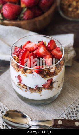 Hausgemachtes Müsli, Müsli mit Schokolade, Erdbeeren und Joghurt im Glas auf rustikalen Holzmöbeln Hintergrund. Gesundes Frühstück. Stockfoto