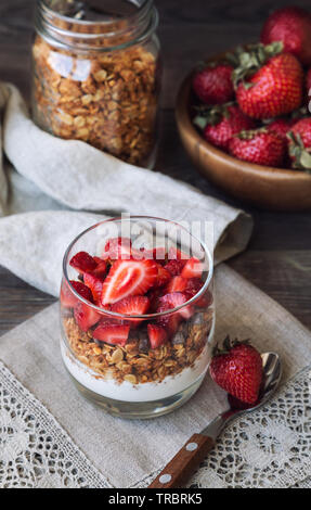 Hausgemachtes Müsli, Müsli mit Schokolade, Erdbeeren und Joghurt im Glas auf rustikalen Holzmöbeln Hintergrund. Gesundes Frühstück. Stockfoto