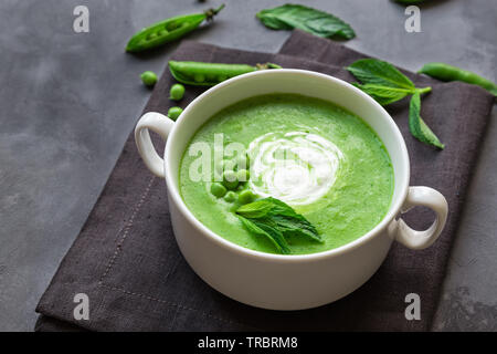 Erbsen und Minze Suppe in Schüssel auf grauem Beton Hintergrund. Stockfoto