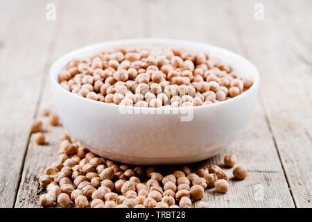 Frische rohe organische Kichererbsen aus weisser Keramik Schüssel auf rustikalen Holztisch Hintergrund. Gesundes Essen. Stockfoto