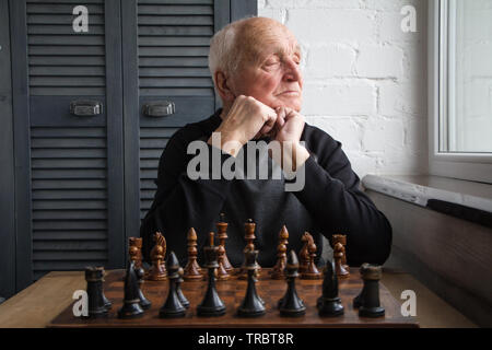 Ein alter Mann sitzt vor einem Schachbrett, Wunder und schaut aus dem Fenster, bevor das Spiel, kopieren Raum Stockfoto