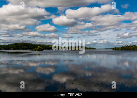 Ferienhaus See mit placid Lake, Cloud Reflexion über Wasser, blauer Himmel mit weißen flauschigen Wolken und grünen Wald Stockfoto