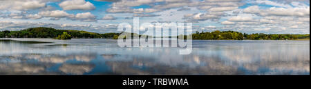 Ferienhaus See mit placid Lake, Cloud Reflexion über Wasser, blauer Himmel mit weißen flauschigen Wolken und grünen Wald Stockfoto