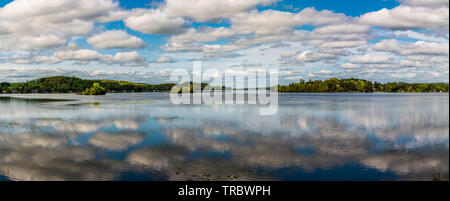 Ferienhaus See mit placid Lake, Cloud Reflexion über Wasser, blauer Himmel mit weißen flauschigen Wolken und grünen Wald Stockfoto