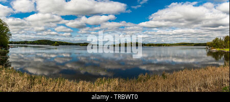 Ferienhaus See mit placid Lake, Cloud Reflexion über Wasser, blauer Himmel mit weißen flauschigen Wolken und grünen Wald Stockfoto