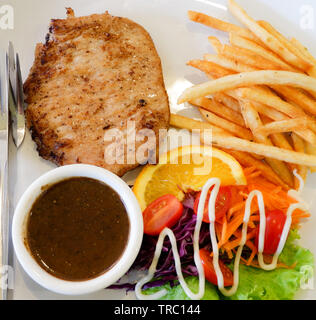 Gegrilltes Steak vom Schwein Pommes frites Salat Gemüse tomate Zitrone mit Steak Sauce auf dem Teller auf dem Tisch Stockfoto