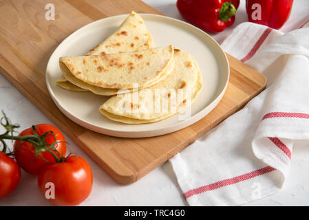 Hausgemachte italienische Piadina auf einem weißen Teller mit Gemüse Tomaten und Paprika auf weißem Hintergrund. Italienische Küche. Ansicht von oben, kopieren Platz für Text. fla Stockfoto