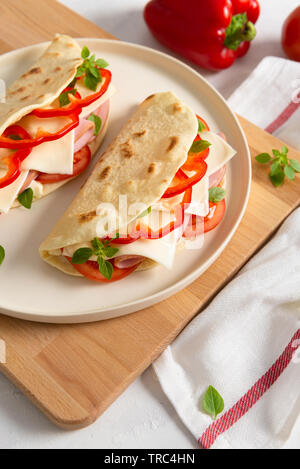 Piadina Romagnola - italienisches Fladenbrot mit Schinken, Tomaten, Basilikum, Paprika und Käse auf weißem Hintergrund. Close Up, vertikal Stockfoto