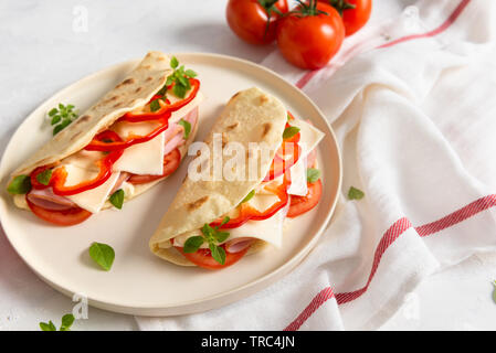 Piadina Romagnola - italienisches Fladenbrot mit Schinken, Tomaten, Basilikum, Paprika und Käse auf weißem Hintergrund. Nahaufnahme Stockfoto