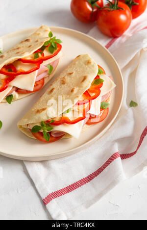 Piadina Romagnola - italienisches Fladenbrot mit Schinken, Tomaten, Basilikum, Paprika und Käse auf weißem Hintergrund. Nahaufnahme Stockfoto