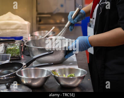 Koch Essen schlagen mit Schneebesen in einer Schüssel aus rostfreiem Stahl Stockfoto