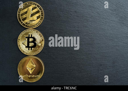 Physische Bitcoin, Litecoin und des Astraleums Gold Münzen auf einen schwarzen Stein Schiefer platte Hintergrund. Cryptocurrency. Kopieren Sie Platz auf der rechten Seite. Stockfoto