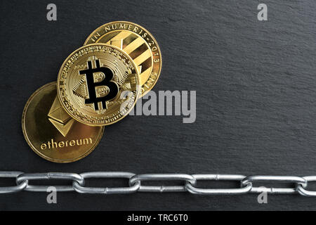 Physische Bitcoin, Litecoin und des Astraleums Gold Münzen auf einen schwarzen Stein Schiefer Platte mit Kette. Cryptocurrency blockchain abstraktes Konzept. Stockfoto