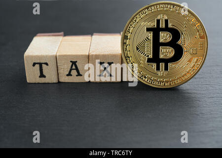 Physische Bitcoin Goldmünze mit Steuer text aus Holzklötzen auf dunklem Stein Schiefer platte Hintergrund. Cryptocurrency Besteuerung abstraktes Konzept. Cop Stockfoto