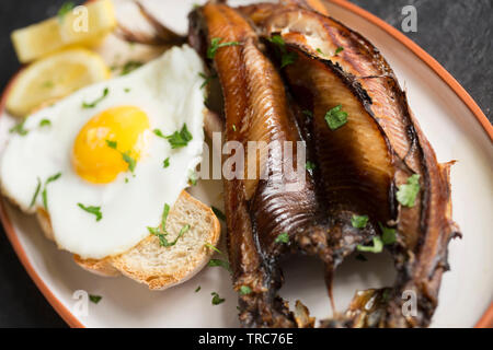 Ein gegrilltes Kaltgeräucherten Craster Kipper aus einem Atlantischer Hering, Clupea harengus, dass zum Frühstück mit einer Scheibe geröstetem sourdo serviert wurde. Stockfoto