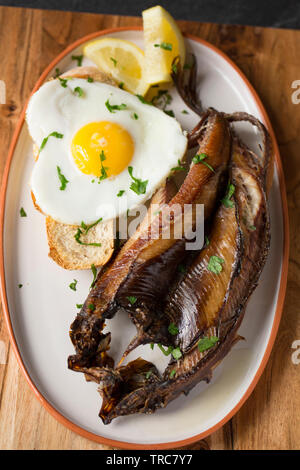 Ein gegrilltes Kaltgeräucherten Craster Kipper aus einem Atlantischer Hering, Clupea harengus, dass zum Frühstück mit einer Scheibe geröstetem sourdo serviert wurde. Stockfoto