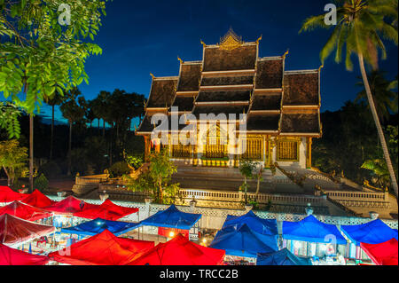 Die Hmong Nachtmarkt mit Haw Pha Bang Tempel im Hintergrund im Zentrum von Luang Prabang, ein Weltkulturerbe Stadt in Laos aufgeführt. Stockfoto